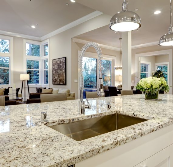 White kitchen design features large bar style kitchen island with granite countertop illuminated by modern pendant lights. Northwest, USA